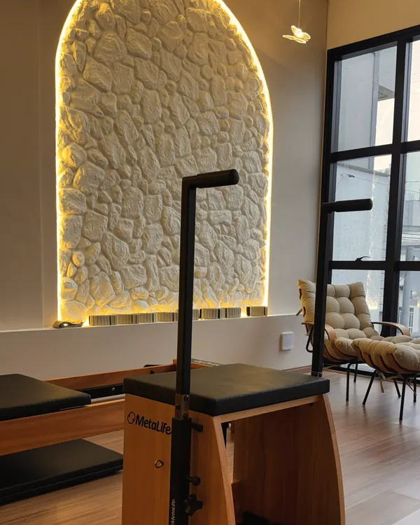 Chair de pilates em madeira diante do nicho de pedra em arco iluminado, na unidade Beira-Mar