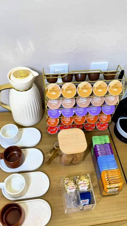 Cantinho do café com garrafa térmica, xícaras, cápsulas de café, chás e biscoitos