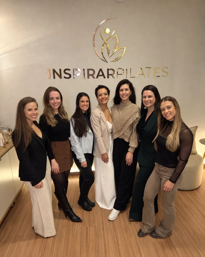 Equipe da Inspirar Pilates reunida em frente ao logo da marca, em dourado e rosé, na recepção