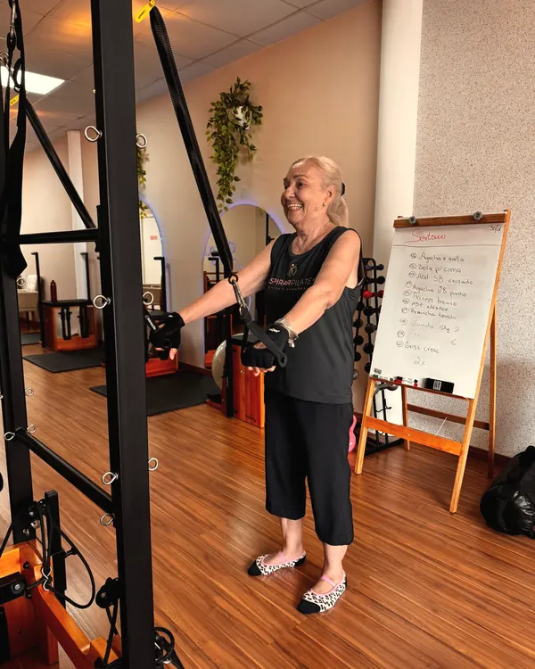 Aluna sorrindo durante exercício com molas na torre, em aula de Pilates Clínico