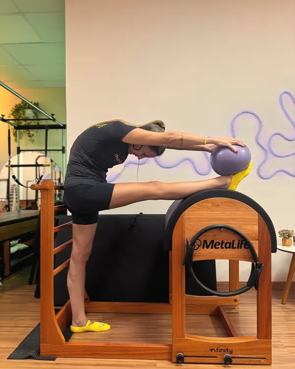 Aluna alongando a perna sobre o ladder barrel com uma bola de pilates